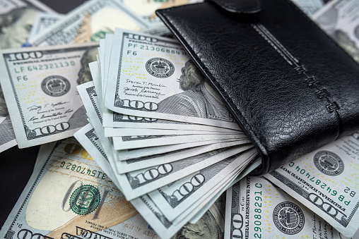 many dollars put in black wallet isolated on black background. Wealth. Abundance. Luxury.
