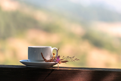 Cup of coffee or tea and bouquet of dried flowers on wooden balcony railing, blurred nature autumn mountain in background with copy space. Slow down, coffee time, rest, relax breakfast outdoor