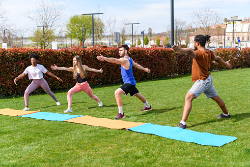 Four People of Different Ethnicities are Stretching Outdoors in Public Park.