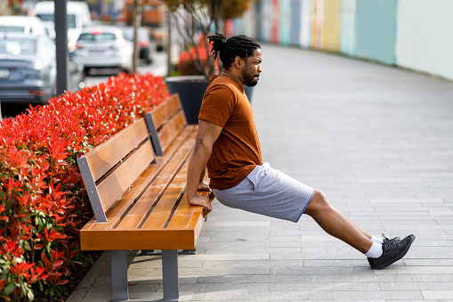 A Young African Man is Doing Work Out in a Public Park on a Park Bench.