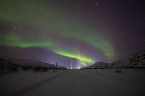 Violet and green Northern lights over dark winter road stock photo