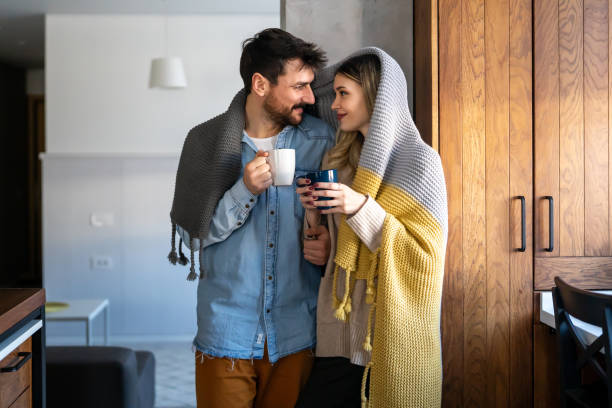 istock Happy young couple with hot drinks cuddling under warm blanket at home 1658818033