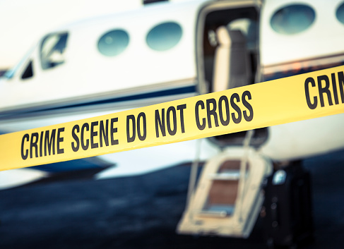 Crime scene cordon tape in front of a small airplane at an airport.