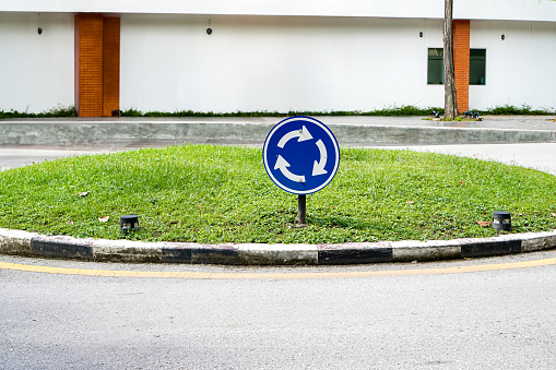 The picture shows a blue roundabout traffic sign located on the lawn in front of the building.