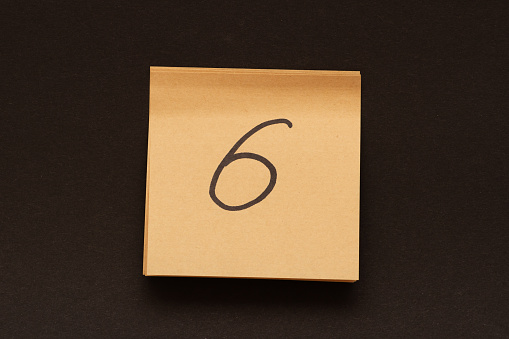 Цифра 6 написанная черным маркером на клеящейся записке. Крупным планом.
