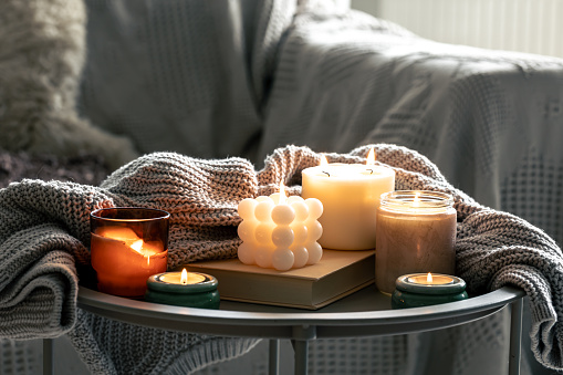 Cozy still life with a set of burning candles and a knitted element on a blurred background of the interior of the room.