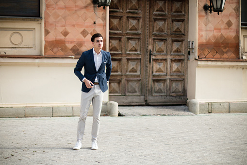 Young elegant businessman in a suit standing in front of an old historic building on the street