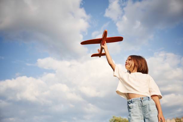 istock Cloudy sky. Happy little girl is playing with toy plane outdoors 1658856467