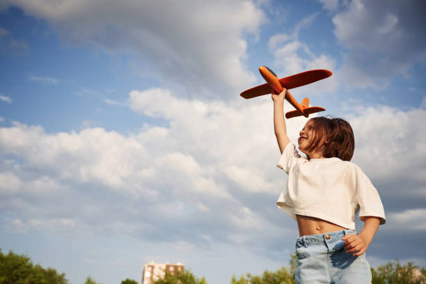 istock Cloudy sky. Happy little girl is playing with toy plane outdoors 1658856487