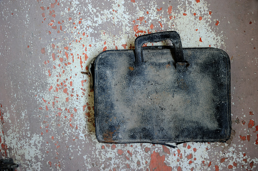 Dirty old briefcase on peeling paint background.