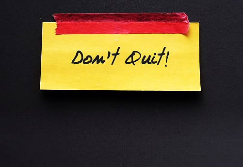 Stick note on copy space black backgroud with handwritten words DON'T QUIT, to encourage to try one more time, never give up and overcome obstacles to be success