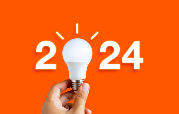 istock Glowing 2024 calendar year numbers, neon style with creative trend light bulb holding by businessman's hand on digital network and orange background. Happy 2024 New Year greeting card with light bulb. 1658861921