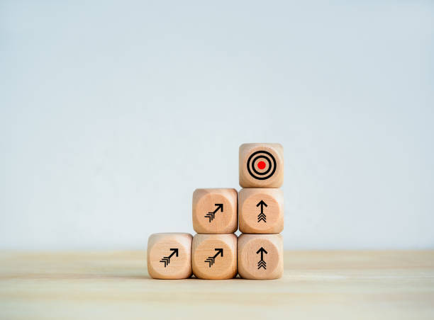 istock Goal target icon and towards arrows symbol on wooden cube blocks as business graph steps on desk, white background. Business growth process, objective goals, dashing to the target, success concepts. 1658862152