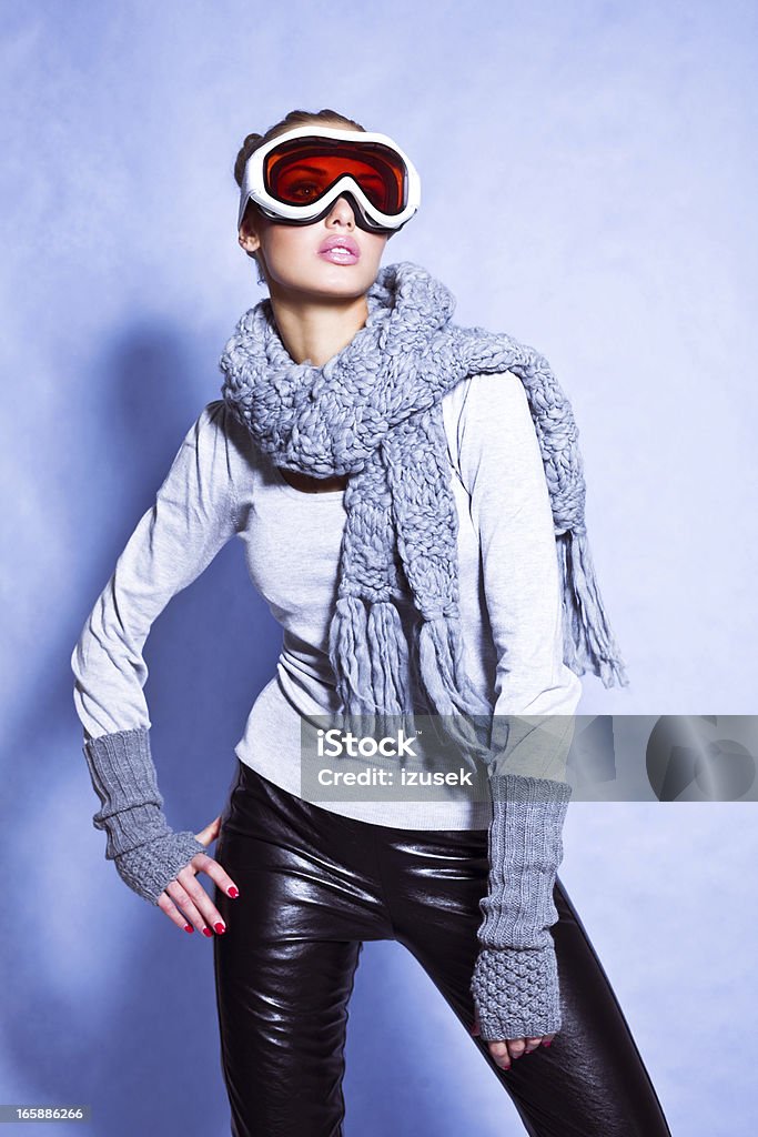Fashion Skier, Winter Portrait Winter portrait of a beautiful young woman wearing goggles and scarf posing against blue background. Studio shot. Snow Stock Photo