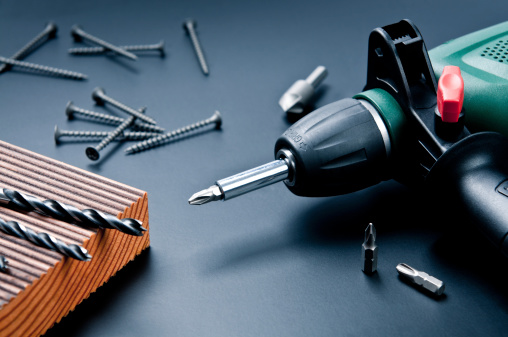 Electric drill with drill bits, screws on dark background