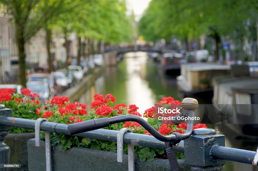 Bicycle on canal bridge A bicycle is parked on a bridge over a canal next to a flower box in Amsterdam, Holland.  House boats are anchored along the canal.  Focus on front handle bar grip with shallow depth of field Amsterdam Stock Photo