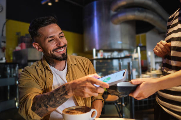 A young man pays with his phone after drinking coffee in a local