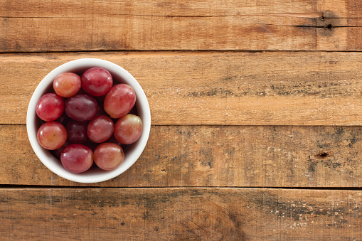 Top view of white bowl full of red grapes over wooden table