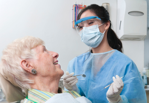 A female dental hygienist smiles and talks with an elderly female patient as she prepares to work on her teeth.  