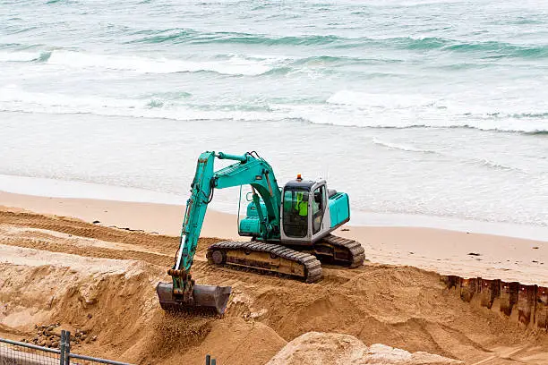 Photo of Excavator working on the beach with ocean, copy space