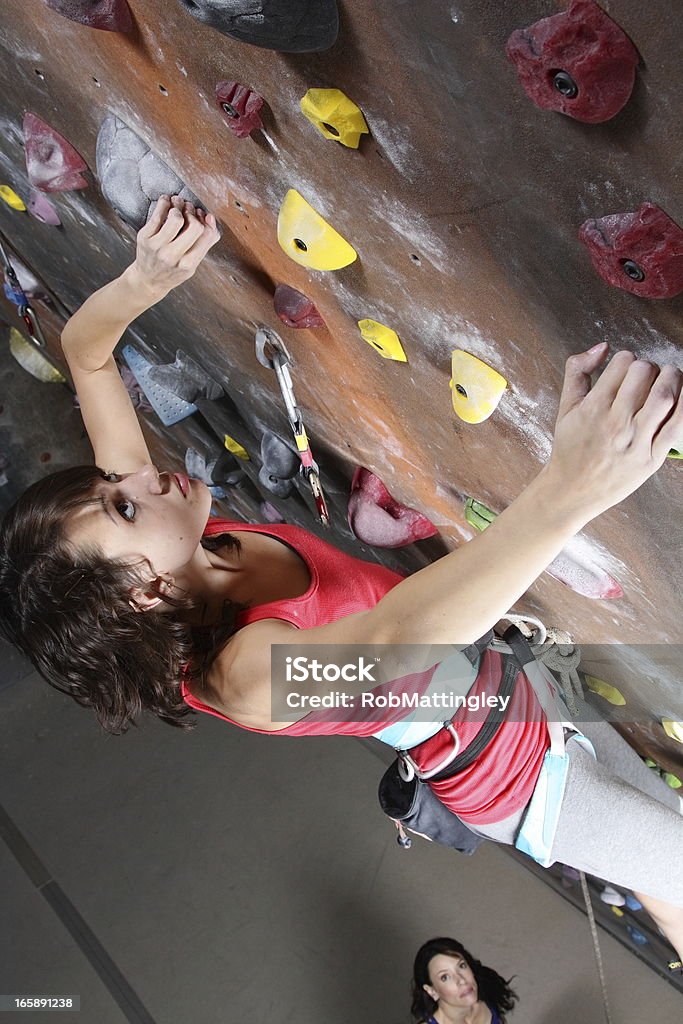 Indoor Rock Climbing A teenage girl scales the wall at an indoor rock climbing location.  A woman can be seen watching her from below. 14-15 Years Stock Photo