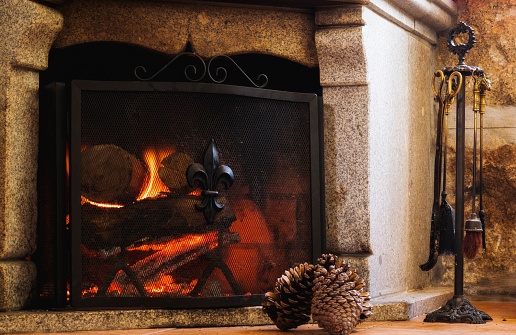 A cozy, traditional woodburning fireplace with a stack of logs and pine cones in front of it