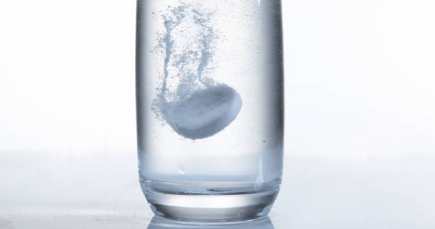 istock Tablets Falling and Dissolving into a Glass of Water against White Background 1658939342