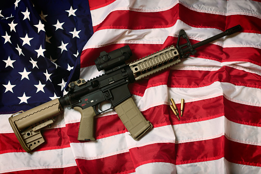 An AR-15 rifle with bullets on an American flag, a symbol of the right of patriotic Americans to bear arms, guaranteed by the Second Amendment.