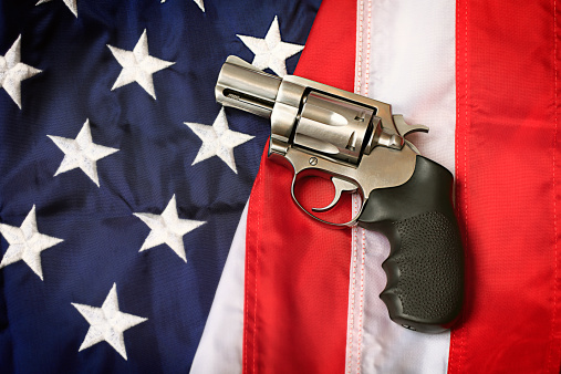 A handgun resting on an American flag, representing the Second Amendment of the US Constitution, the right of patriotic Americans to bear arms. Social issues concept.