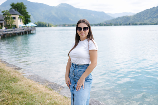 Beautiful female in denim skirt posing to photographer in front of big beautiful lake with clear water. High quality photo