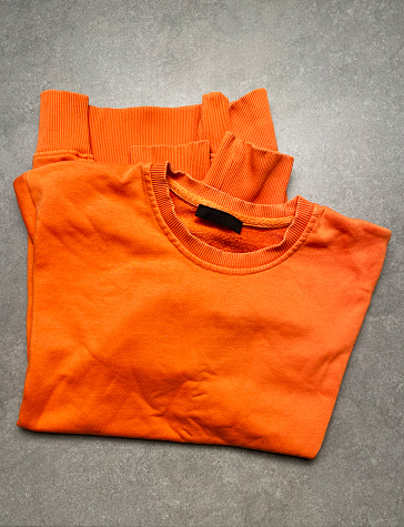 Sweatshirt. Directly above a folded orange color sweatshirt on gray color background