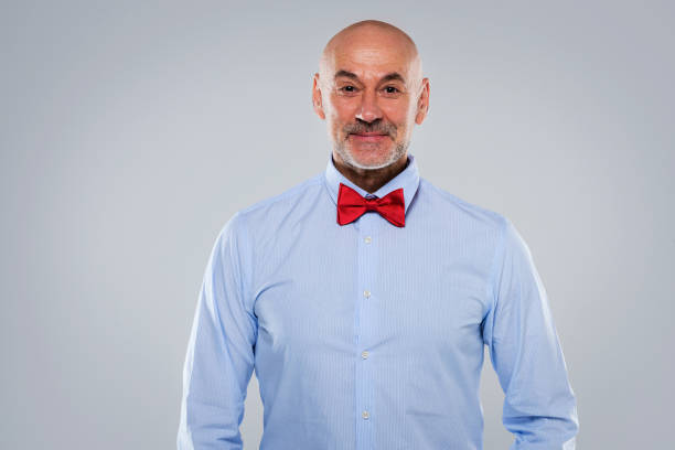 портрет мужчины средних лет в рубашке и галстуке-бабочке, стоящего на изолированном сером фоне - bow looking at camera waist up indoors стоковые фото и изображения