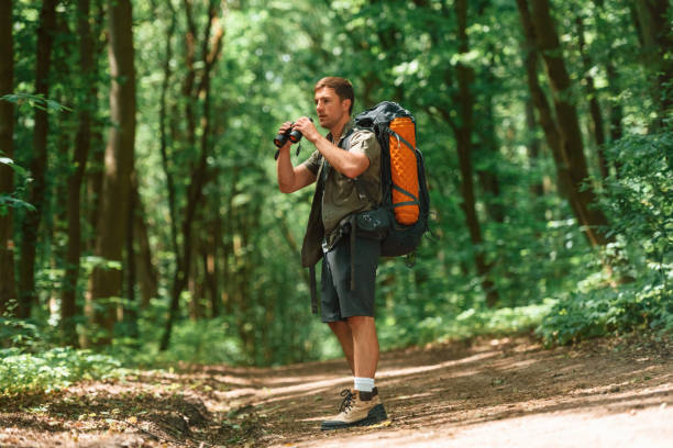 istock Standing and holding binoculars. Tourist in summer forest. Conception of exploration and leisure 1658972704