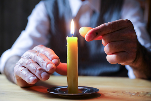 Close-up view of male fingers near yellow candle flame.