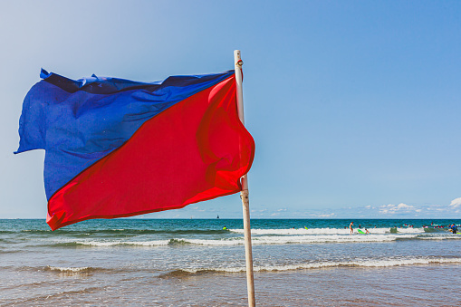 Red and blue flag on the beach against the backdrop of people swimming in the sea