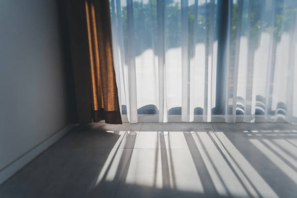 Sun rays penetrate the room through transparent white curtain tulle on a sunny day, interiors details stock photo