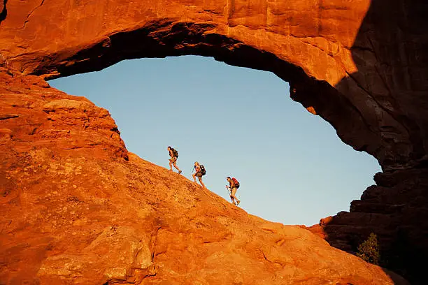 Three hikers explore the North Window at sunrise in Arches National Park.
