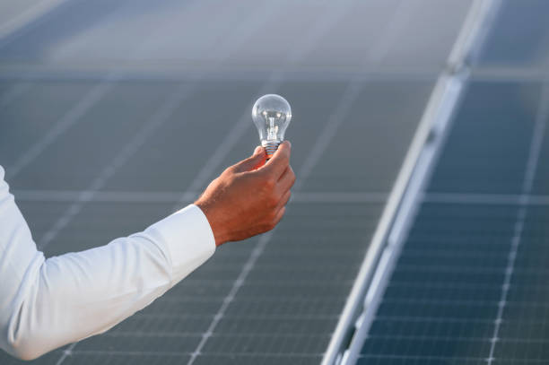 istock Close up view of man's hand that is holding light bult in front of solar panel 1659051657