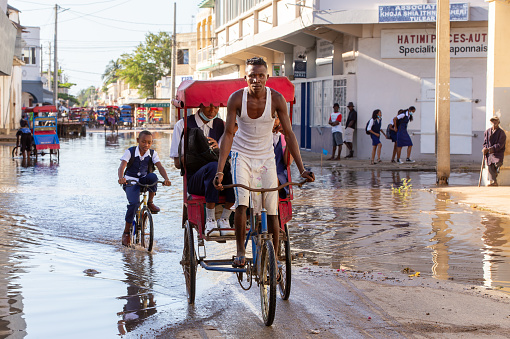 Toliara, Madagascar - November 21. 2022: Traditional rickshaw bicycle with Malagasy passengers on the street, one of the ways to earn money. Everyday life on the cities street of Madagascar.