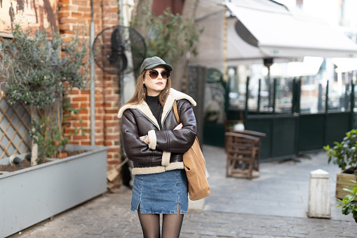 Portrait of a beautiful young fashionable woman wearing a cap and shearling jacket in the city street on a lovely autumn day in Thessaloniki