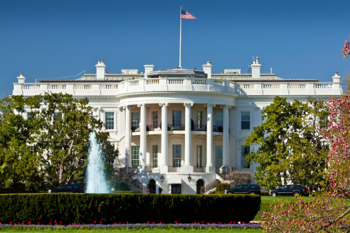 Washington DC, USA - March 12, 2012: Front of the White House with a fountain in the gardens. A man in black walks on the roof, security staff and other staff in the grounds. 