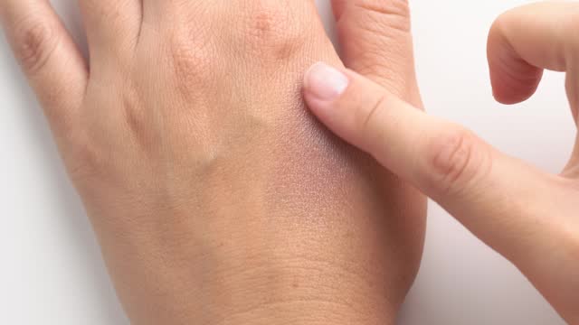 Close up shot of woman applying eyeshadow on hand skin. Eyeshadow smeared with a finger on the hand
