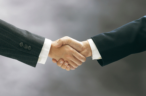 Two women are shaking hands in the office meeting. People behind are blurred.