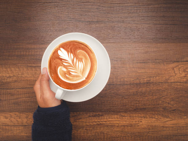 istock Hand woman holding a fresh coffee cup over wooden table 1659064553