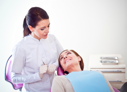 A dentist explains something to her patient sitting in the examination chair.