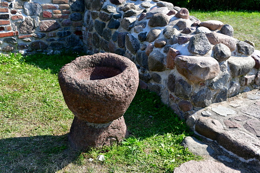 A close up on a wooden bowl or chalice being a remnant of a medieval chapel seen next to ruins of the walls made out of rock, stone, or boulder set connected with some plaster seen on a sunny day