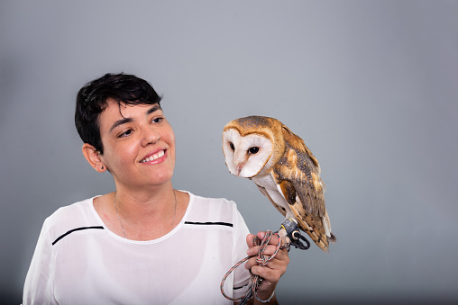 A woman lovingly looking at her owl. Wild animal. Against gray background.