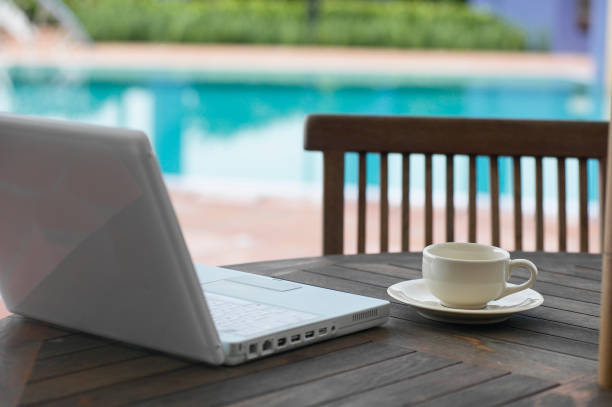 istock Coffee cup and a laptop on a table with pool side view. 1659094506