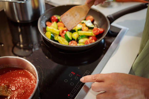 istock Woman adjusting temperature in a stove top while cooks vegetables 1659098173