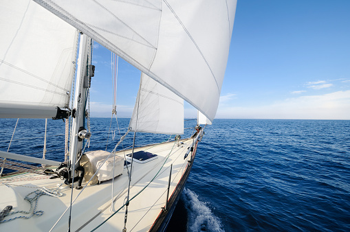 Regatta sailing ship yachts with white sails at opened sea. Aerial view of sailboat in windy condition.